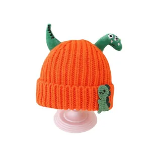 Children's bright orange knitted hat with green dinosaur horns and cartoon patch