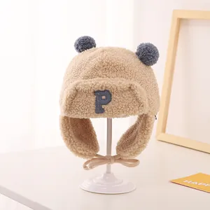 Detailed view of beige fleece trapper hat with blue pom-poms and P letter patch for kids