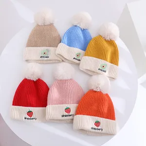 Flat lay of colorful children's knit hats with fruit embroidery and soft pom-poms