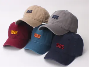 Detailed view of five cotton baseball caps with 1985 embroidery in multiple colors