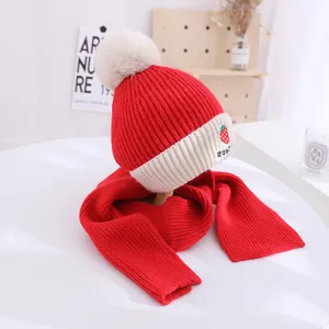 Detail of red knitted kids winter hat and scarf set featuring strawberry embroidery