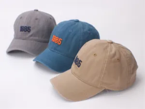 Detailed view of washed cotton baseball caps with 1985 embroidery in multiple colors