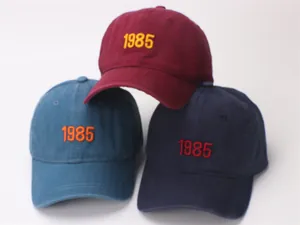 Detail view showing three washed cotton baseball caps with 1985 embroidery in multiple colors
