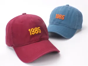 Detail of 1985 embroidery on washed cotton retro baseball caps in red and blue