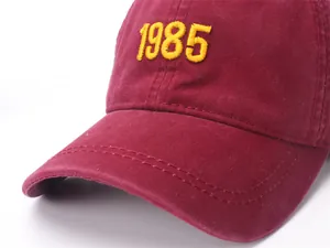 Detail of burgundy baseball cap featuring yellow 1985 embroidery and cotton twill fabric