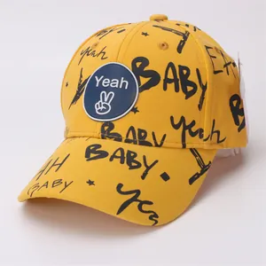 Detail of yellow cotton kids baseball cap featuring black graffiti text and round logo patch