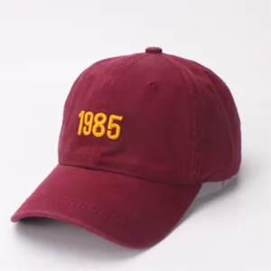 Detailed close-up of dark red cotton baseball cap with yellow 1985 embroidery details