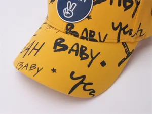 Close-up of yellow cotton baseball cap with black graffiti letters and blue hand patch