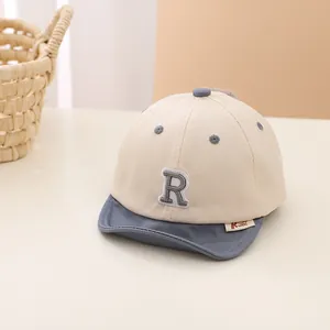 Close-up of beige and blue baby baseball cap with soft brim and embroidered R letter