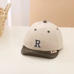 Detail of baby soft-brim baseball cap showing letter R patch and olive green contrast trim