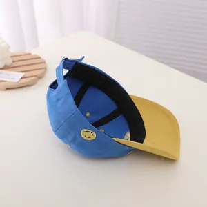 Detail of kids baseball cap featuring blue canvas, yellow brim, and smile embroidery