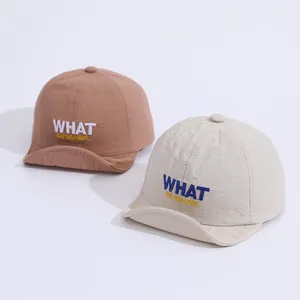 Detail view of two quick-dry baby baseball caps with WHAT embroidery in beige and brick red