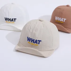 Detailed view of quick-dry kids baseball caps in white, beige and brown with WHAT embroidery
