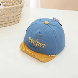 Détail de casquette bébé avec broderie ours et bord souple en bleu marine et jaune