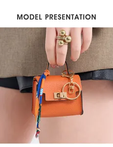 Mini orange leather bag charm with floral silk scarf and gold ring held by a model