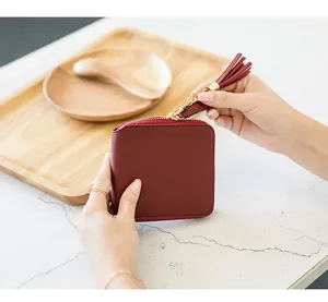 Detail of square wine red leather wallet with gold zipper and stylish tassel charm