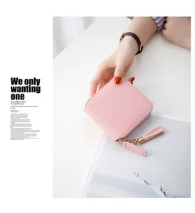 Detail of light pink square wallet featuring a gold zipper and decorative leather tassel