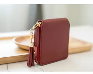 Detail of burgundy leather square wallet featuring gold zipper and stylish tassel charm