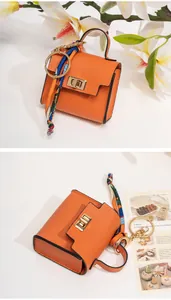 Close-up of mini orange leather bag keychain with golden hardware and silk scarf decoration