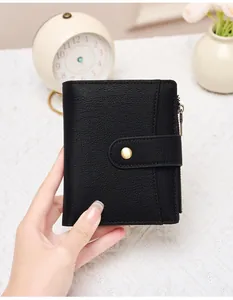 Detail of a black pebbled leather wallet with a gold snap button being held by hand