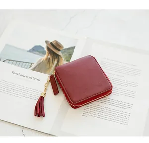 Detail of burgundy leather wallet with lychee texture, golden zipper and tassel accent