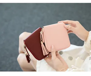 Close-up of burgundy and pink square PU leather wallets with tassels held by a model