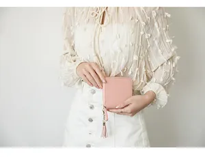 Pink minimalist square wallet with long tassel zipper held by a model in a casual setting