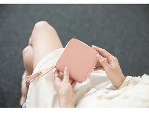 Close-up of pink square zipper wallet with leather tassel detail in woman's hand
