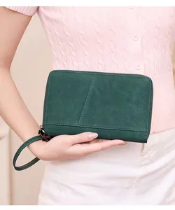 Close-up of green matte leather passport wallet with wrist strap held by a model