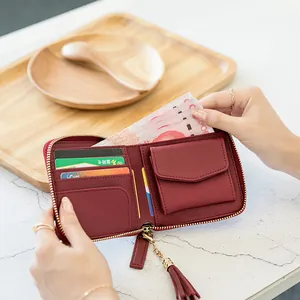Deep red square women's zip wallet with tassel detail on a textured table background