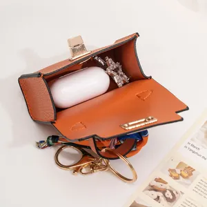 Orange mini bag charm for wireless earbuds with stylish scarf wrap handle and gold clasp