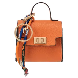 Mini orange leather handbag keychain with silk scarf and golden hardware on white background