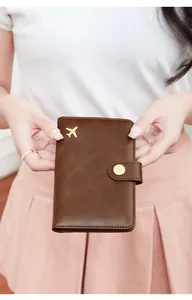 Detail of a brown leather RFID passport holder featuring a golden airplane emblem and buckle