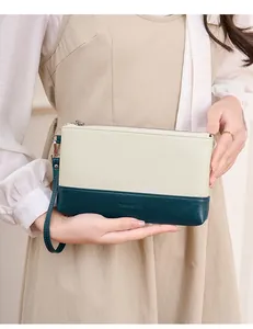Détail d'une pochette bicolore avec surpiqûres précises et logo gravé sur le cuir