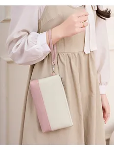Détail d'une pochette bicolore rose et beige avec dragonne portée par un mannequin
