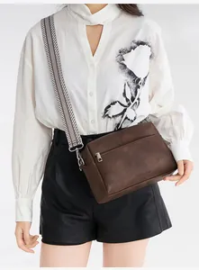 Detail of a brown leather crossbody bag with a wide black and white woven strap