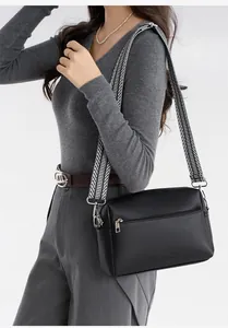 Detail of black pebbled leather crossbody bag with stylish black and white woven strap