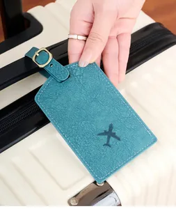 Close-up of a teal lychee leather luggage tag with aircraft icon on a suitcase