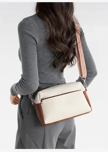 Detail of two-tone crossbody bag with wide woven strap and rear zipper pocket on grey sweater