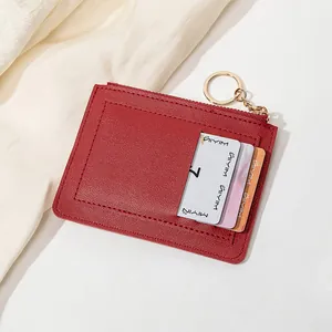 Détail d'un porte-cartes en cuir rouge foncé avec texture fine, zip doré et porte-clés