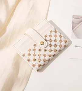 Close-up of cream leather mini wallet featuring brown clover pattern and gold snap button