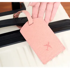 Close-up of pink PU leather luggage tag with airplane motif on a white striped suitcase