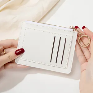Détail d'un porte-cartes ultra-plat en cuir blanc avec porte-clés doré et fermeture éclair