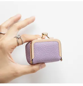 Gros plan d'une mini pochette à bijoux en cuir violet avec fermoir doré tenue à la main