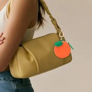 Porte-monnaie en forme d'orange avec feuille verte et porte-clés doré sur un sac