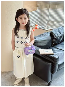 Dettaglio del ricamo floreale blu su un completo da bambina in due pezzi bianco sporco