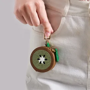 Mini porte-monnaie kiwi avec fermoir doré accroché à la poche d'un jean en denim blanc