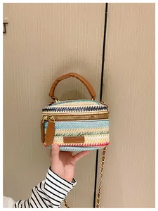 Close-up of woven rainbow straw bucket bag with brown leather handle and gold chain strap
