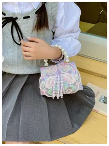 Detail of embroidered floral bag for girls featuring pearl handle and tassel accents