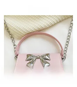 Close-up of pink PU leather handbag featuring a large silver metal bow detail and chain strap